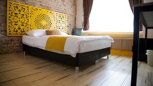Een bed met een wit-geel beddegoed, een zwart hoofdbord en een decoratief geel paneel aan de muur.