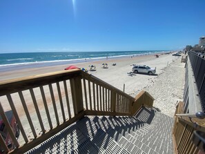 Eine Holzterrasse mit Blick auf einen Strand, eine Sandküste und den Ozean.