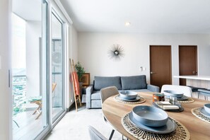 A modern living room with a dining area, large windows, and a view of the city.