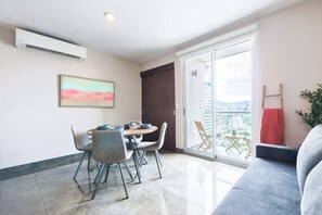 A modern living room with a dining area, a large window with a city view, and a balcony with a red towel.