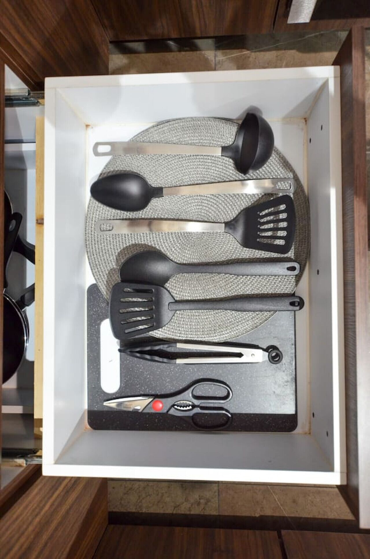 A drawer containing kitchen utensils including a spatula, tongs, and a pair of scissors.