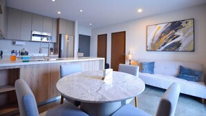 A modern kitchen with a marble island, a dining area with a round table, and a living area with a sofa and a painting. - ¡Moderno y de lujo! - Fundidora, Cintermex, arena (Monterrey)