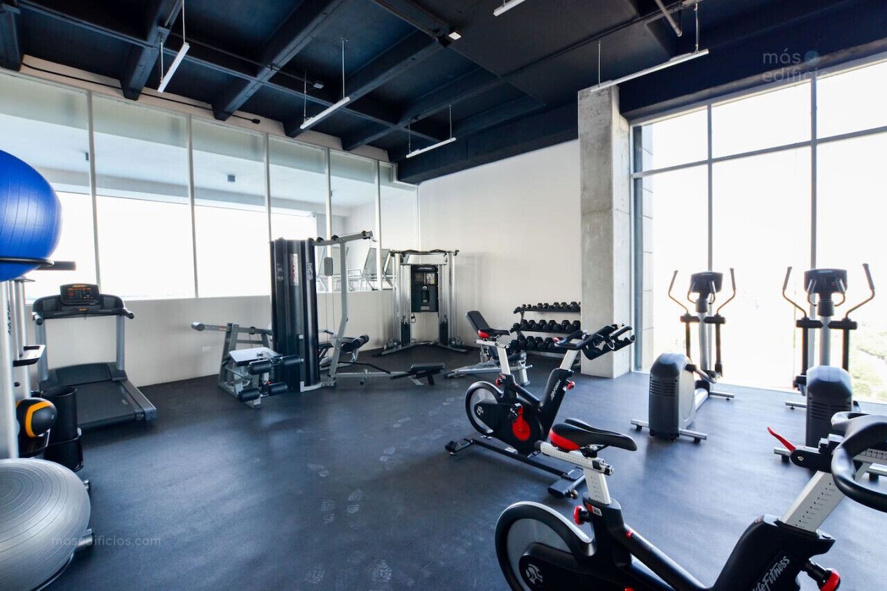Ein Fitnessraum mit Trainingsgeräten, Laufband und einem großen Fenster für natürliches Licht.