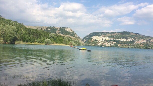 Un lago con barcos, una orilla rocosa y colinas al fondo.