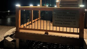 Eine Holztreppe führt zu einer Terrasse, auf der ein Schild die Richtung zu verschiedenen Orten anzeigt.