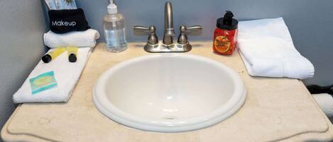 A bathroom sink with a mirror above it, a towel, a bottle of hand soap, a bottle of hand sanitizer, and a bottle of pumpkin spice body wash.