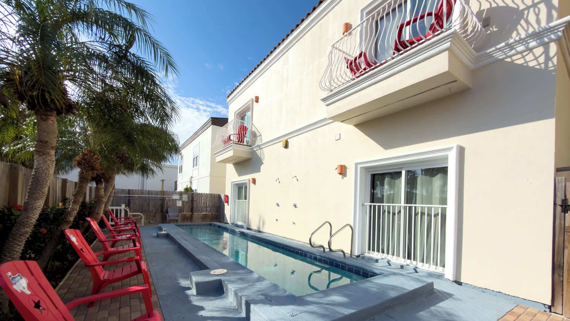 Ein Pool mit roten Liegestühlen, einer Palme und einem Gebäude mit Balkon.