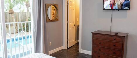A bedroom with a bed, a wooden dresser, a TV on the wall, and a door leading to another room.