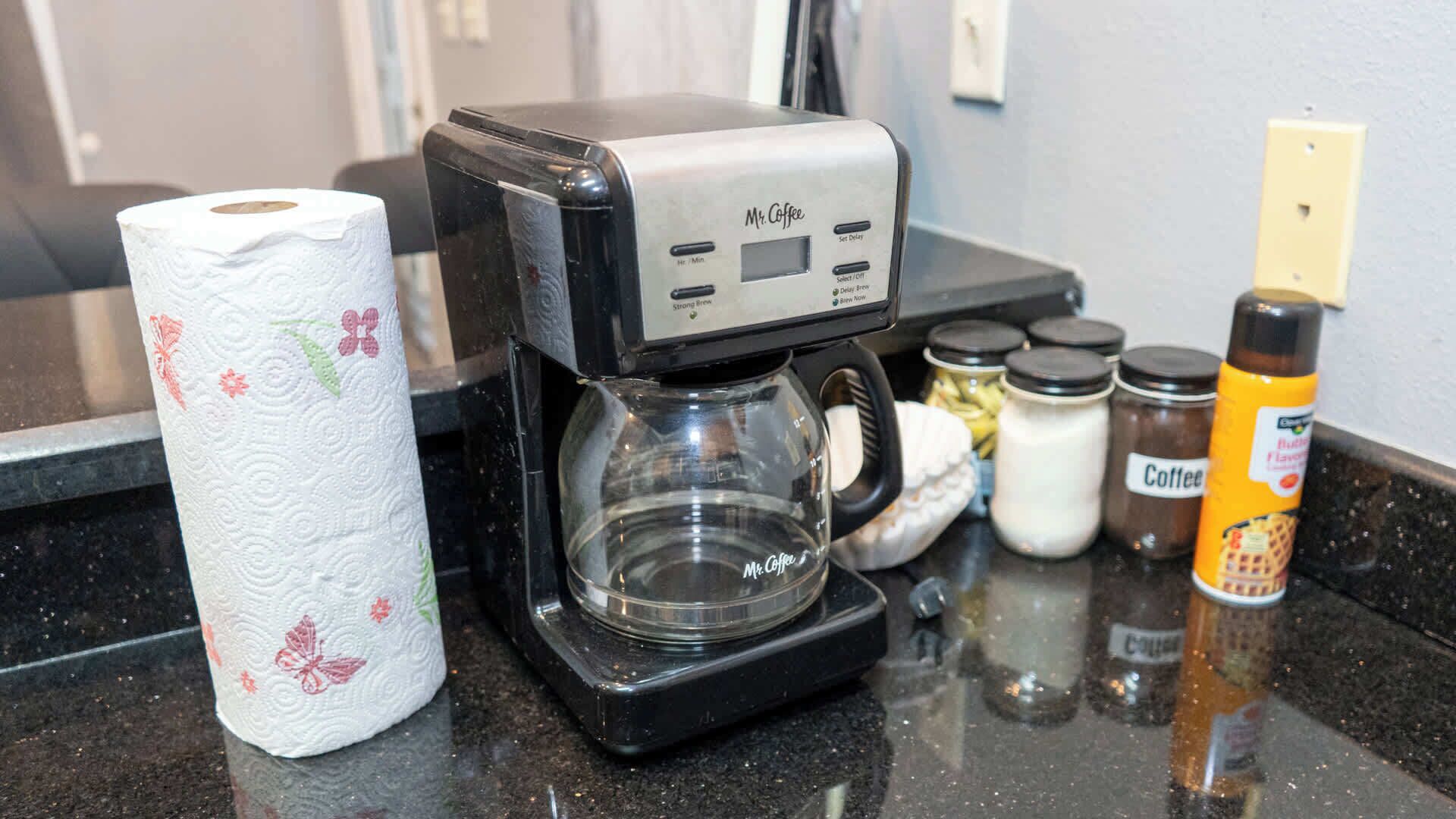 A coffee maker, a roll of toilet paper, and various coffee-related items on a kitchen counter.