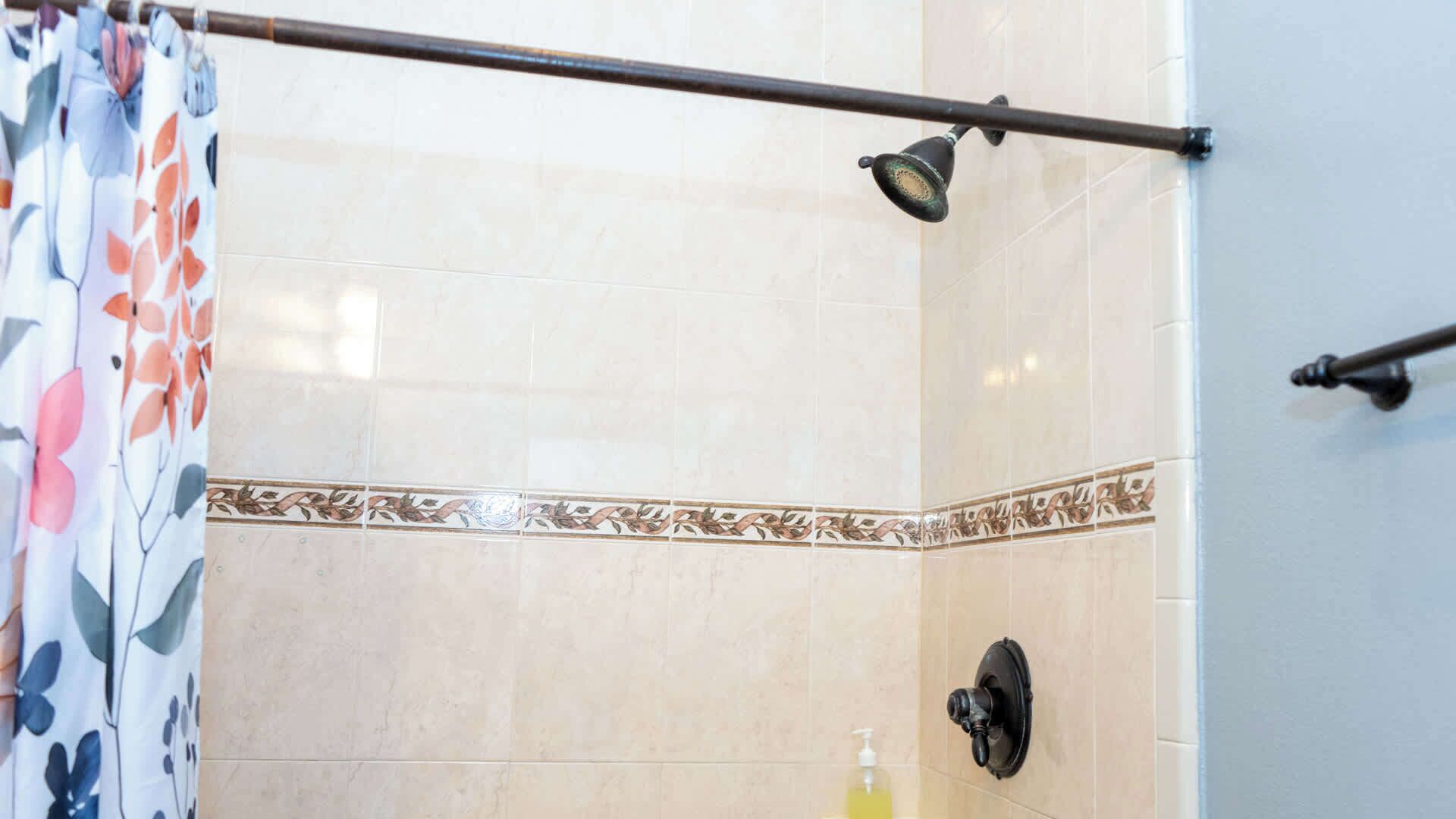 A shower area with beige tiles, a floral curtain, and a handheld showerhead.
