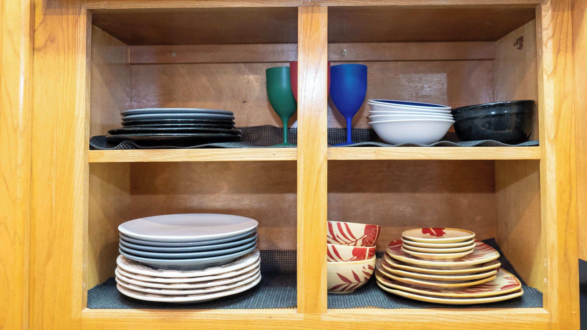 A wooden cabinet with four shelves, each holding stacks of plates and bowls.