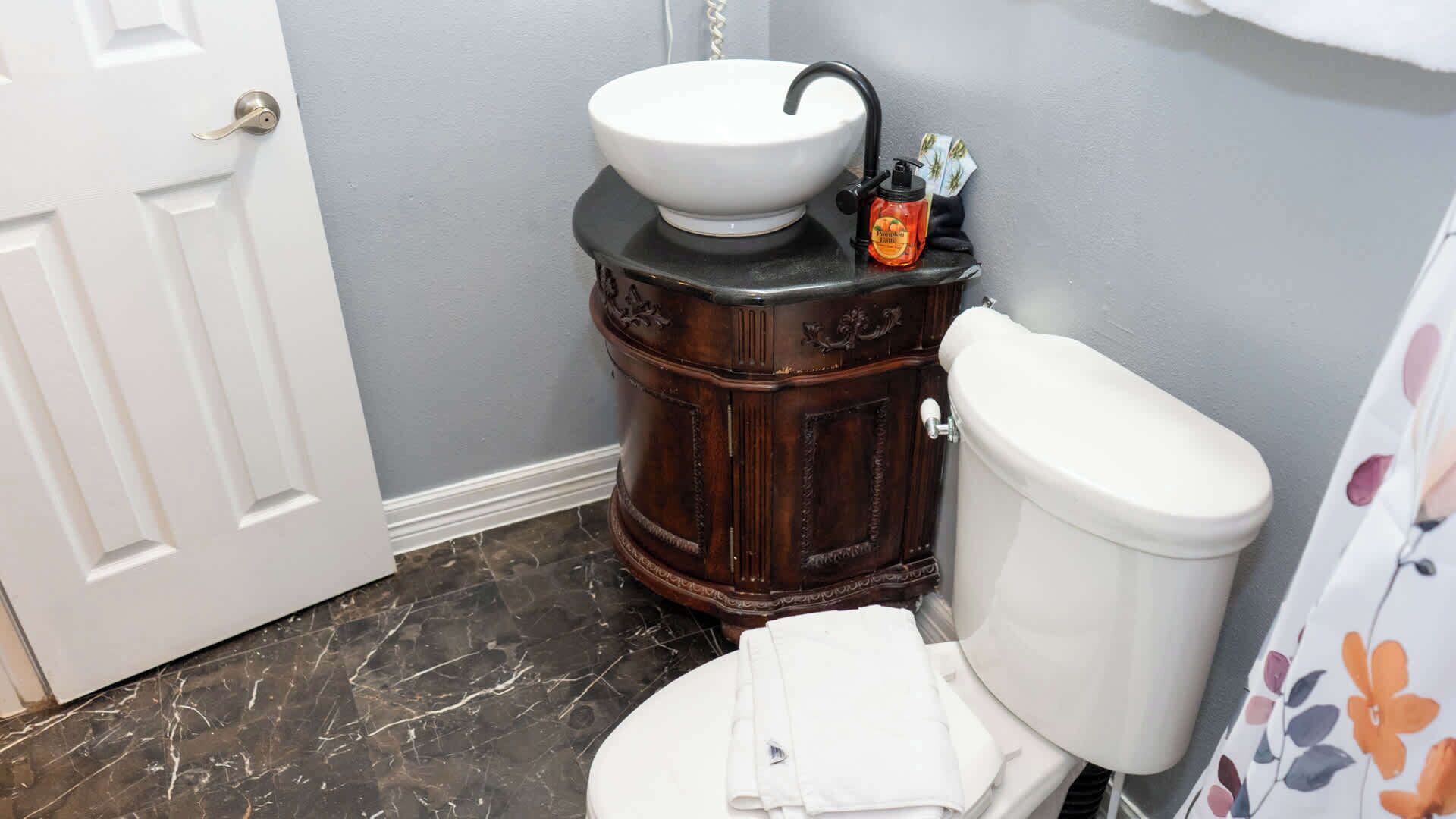 A bathroom with a white toilet, a white sink on a dark wooden vanity, and a shower curtain with a floral pattern.
