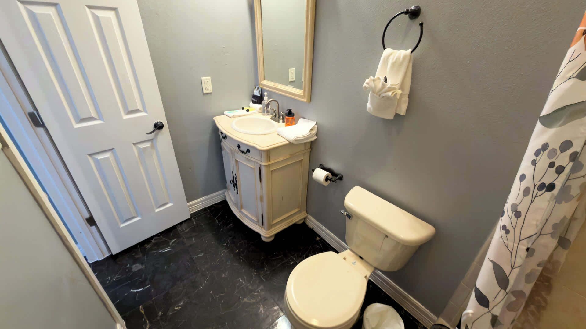 Une salle de bain avec des toilettes blanches, un lavabo surmonté d’un miroir et une serviette accrochée à un crochet.