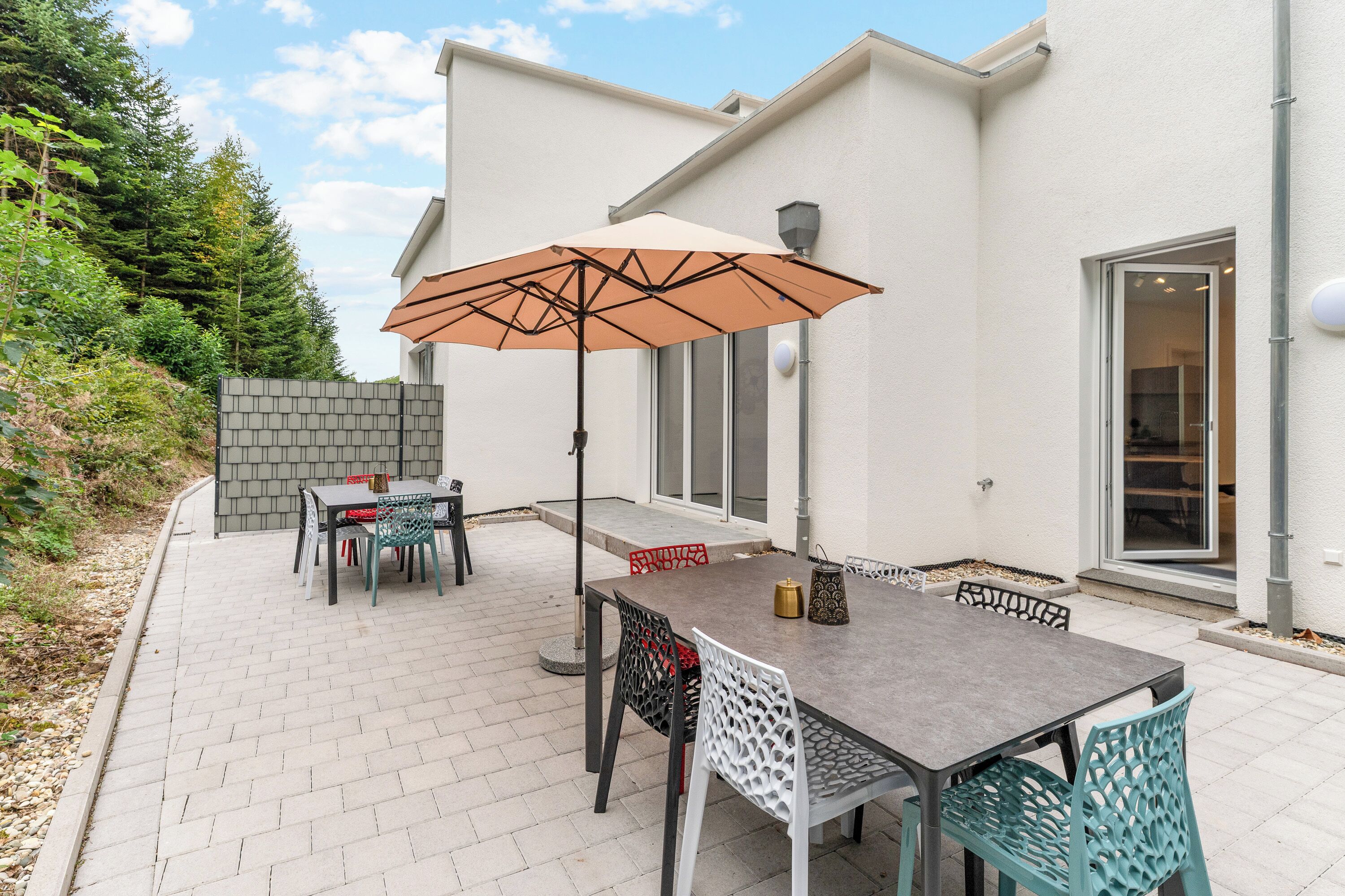 An outdoor patio with a table and chairs, a large umbrella, and a view of a house with a brick wall and a window.