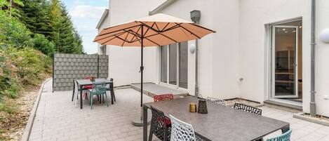 An outdoor patio with a table and chairs, a large umbrella, and a view of a house with a brick wall and a window.