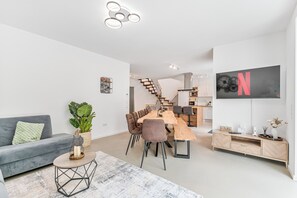 A modern living room with a grey sofa, a wooden dining table, and a staircase leading to a kitchen. - LUMIFLATS Offenbrug (Offenburg)