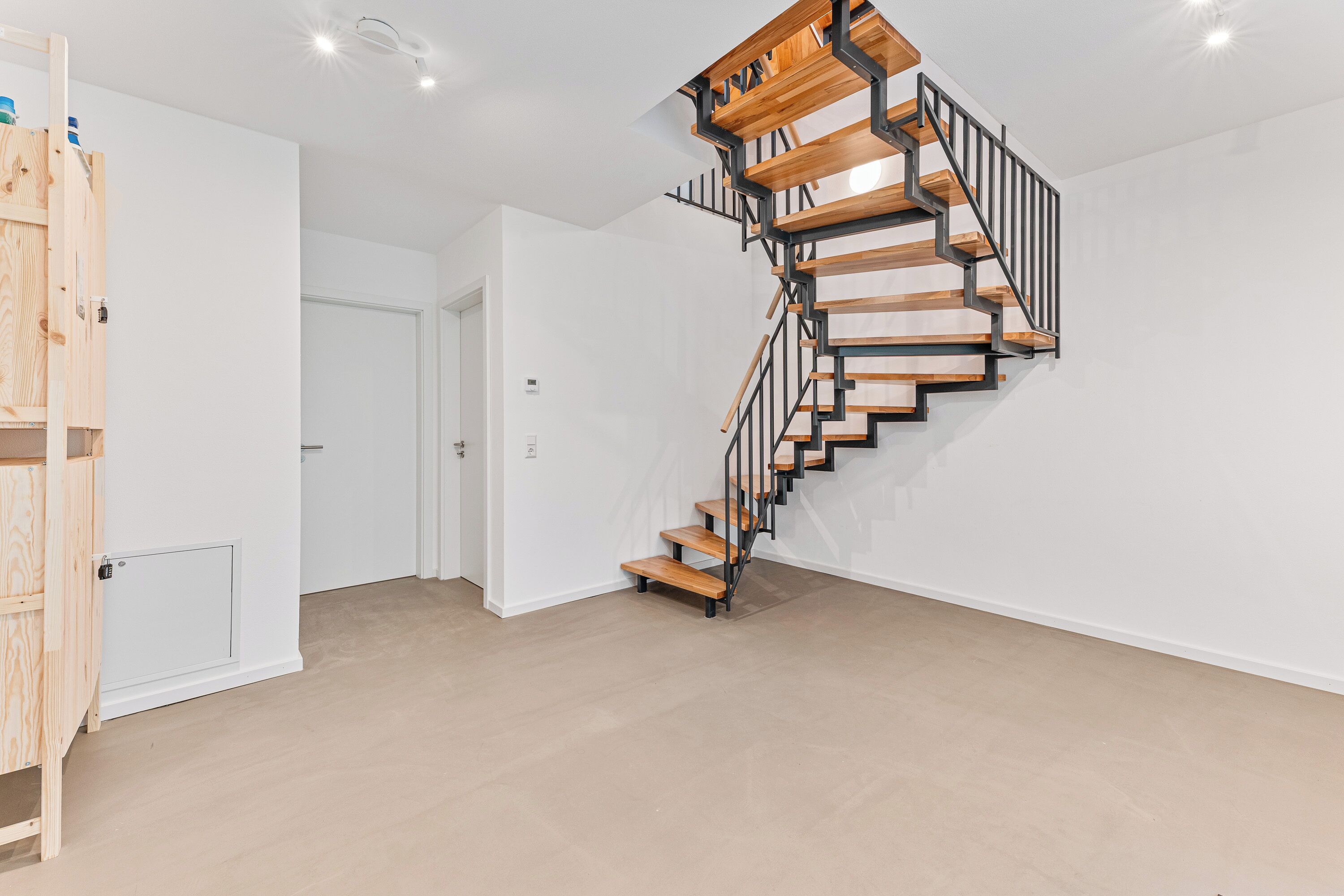 A spiral staircase with wooden steps and black railings in a room with white walls and a wooden floor.