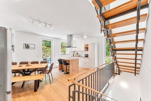 A modern kitchen with a central island, wooden flooring, and a staircase with wooden railings. - LUMIFLATS Offenbrug (Offenburg)