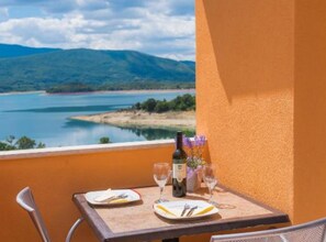 Ein Tisch, gedeckt mit Tellern, Besteck, einer Weinflasche und Gläsern, mit Blick auf einen See und Berge.