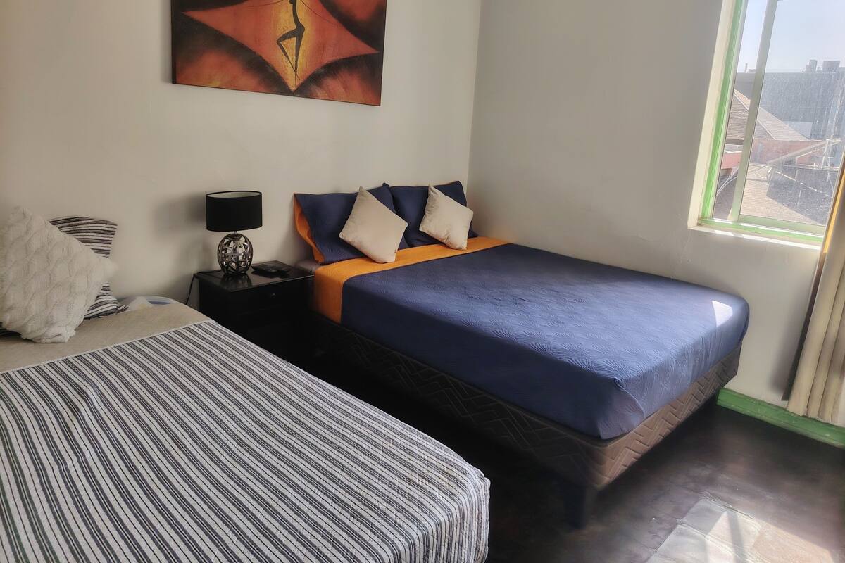 A hotel room with a large bed, a smaller bed, a nightstand with a lamp, and a painting on the wall.