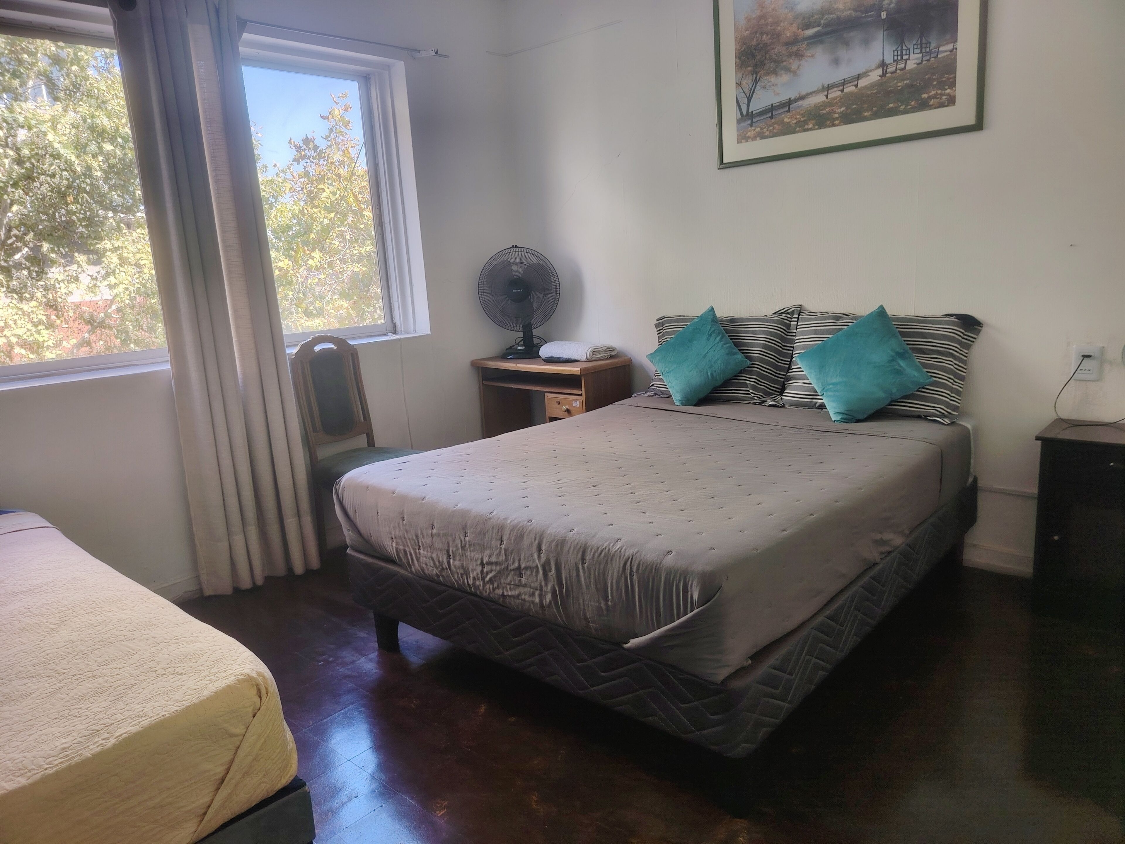 Un dormitorio con cama, escritorio, silla, ventilador y ventana con cortinas.