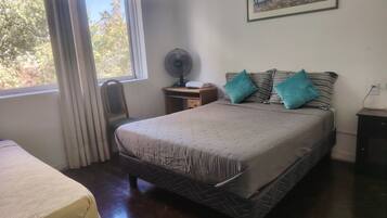 Un dormitorio con cama, escritorio, silla, ventilador y ventana con cortinas.