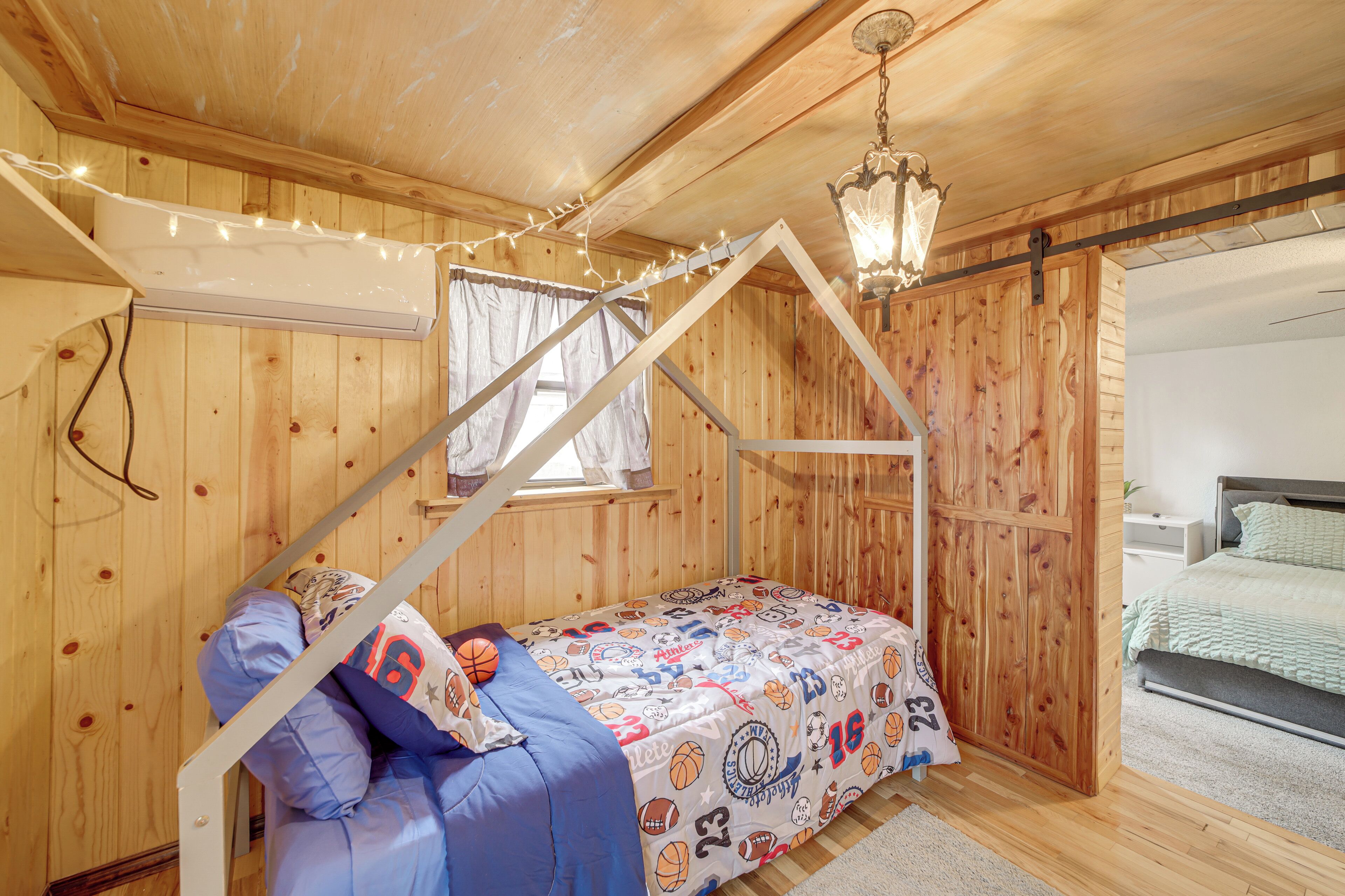 A wooden cabin bedroom with a bunk bed, string lights, and a chandelier.