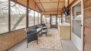 Ein überdachter Außenbereich mit Deckenventilator, Korbmöbeln, einem Fernseher und großen Fenstern.