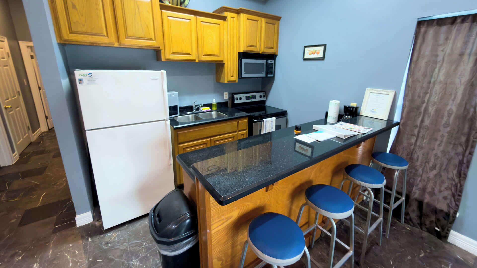 A compact kitchen with wooden cabinets, a refrigerator, a microwave, a stove, and a small island with bar stools.