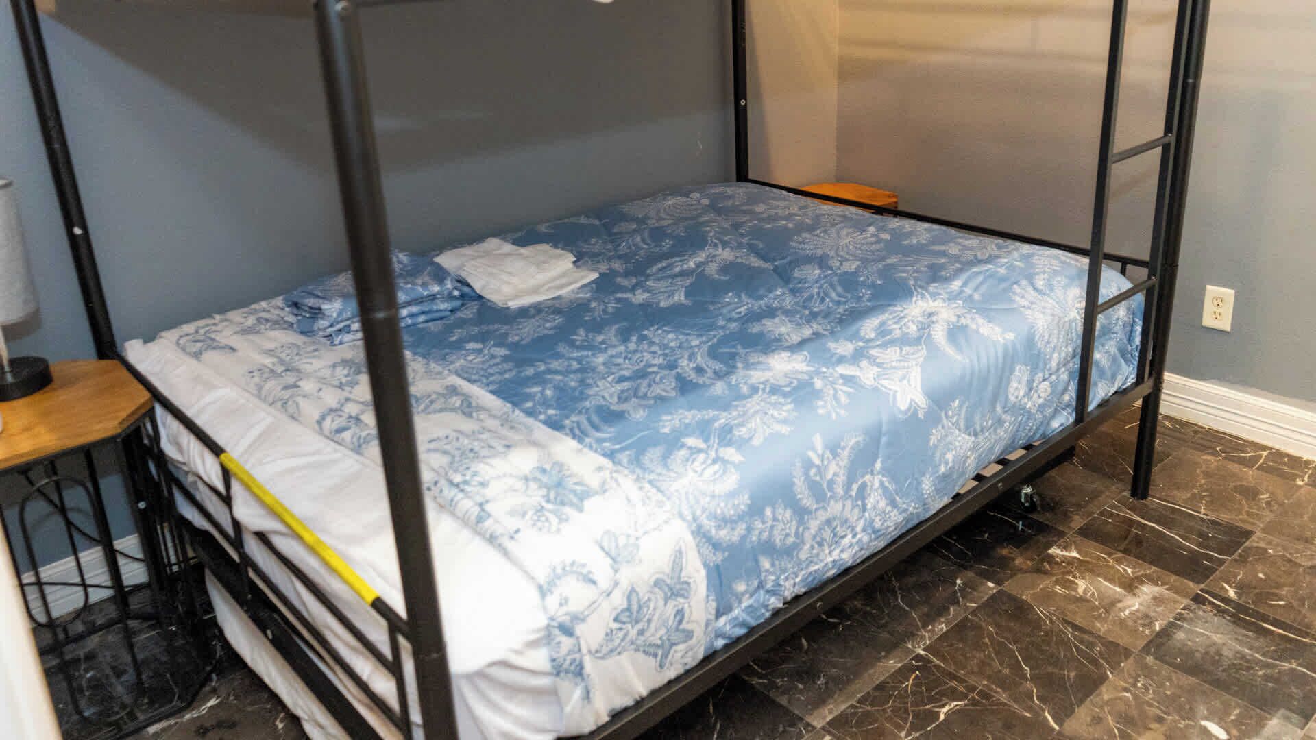 A bunk bed with a patterned bedspread, a small wooden table, and a lamp.
