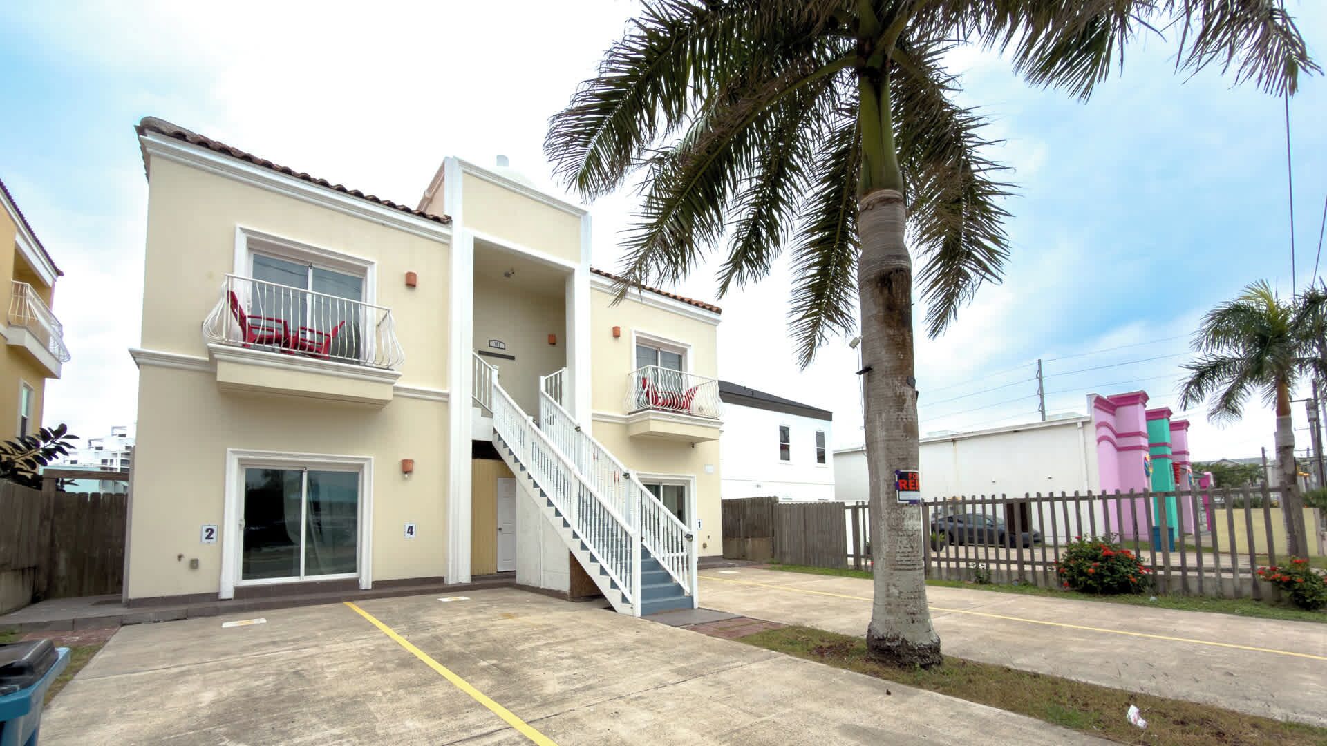 A two-story residential building with a balcony, a staircase, and a parking area.