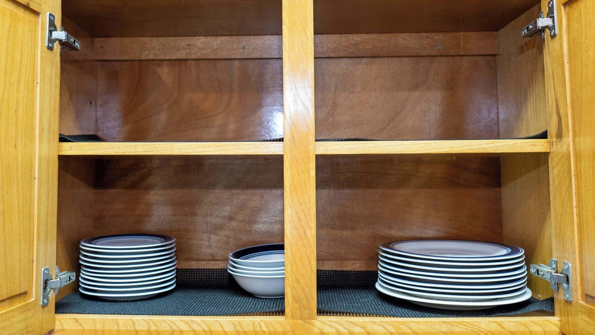 A wooden cabinet with two shelves, each holding stacks of plates and bowls.