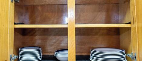 A wooden cabinet with two shelves, each holding stacks of plates and bowls.