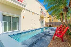 A pool area with a clear blue pool, red lounge chairs, and a palm tree. - Priced Right Near Beach Well Equipped (South Padre Island)