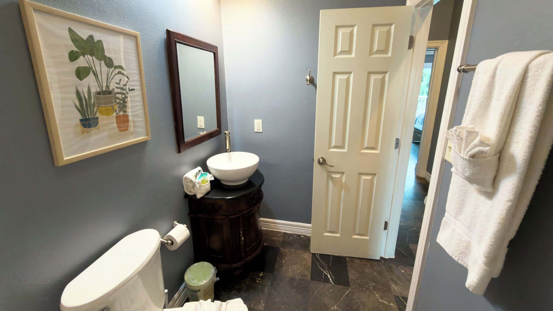 A bathroom with a toilet, sink, mirror, and a door leading to another room.