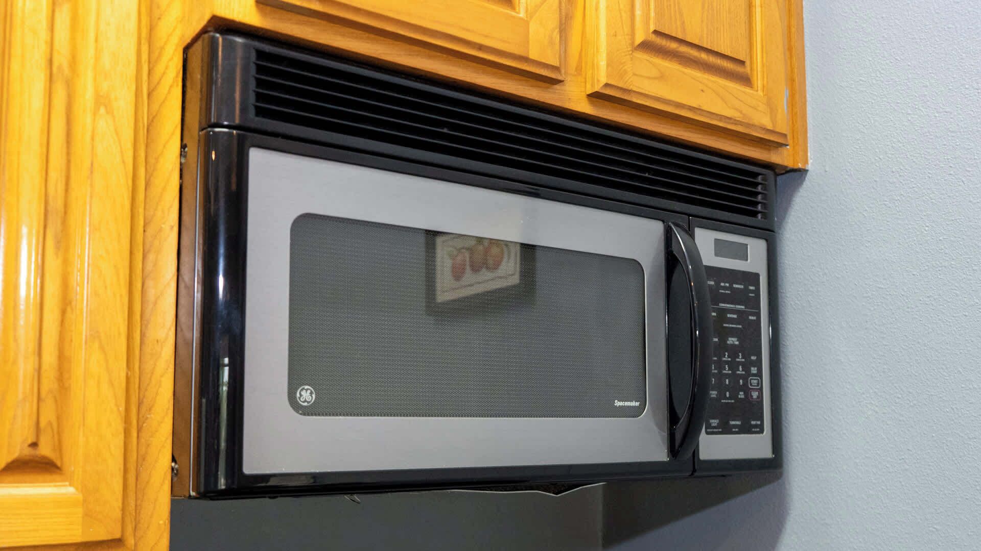 Ein GE Mikrowellenofen mit digitalem Display und Bedienfeld, eingebaut in eine Küche mit Holzschnitzereien.