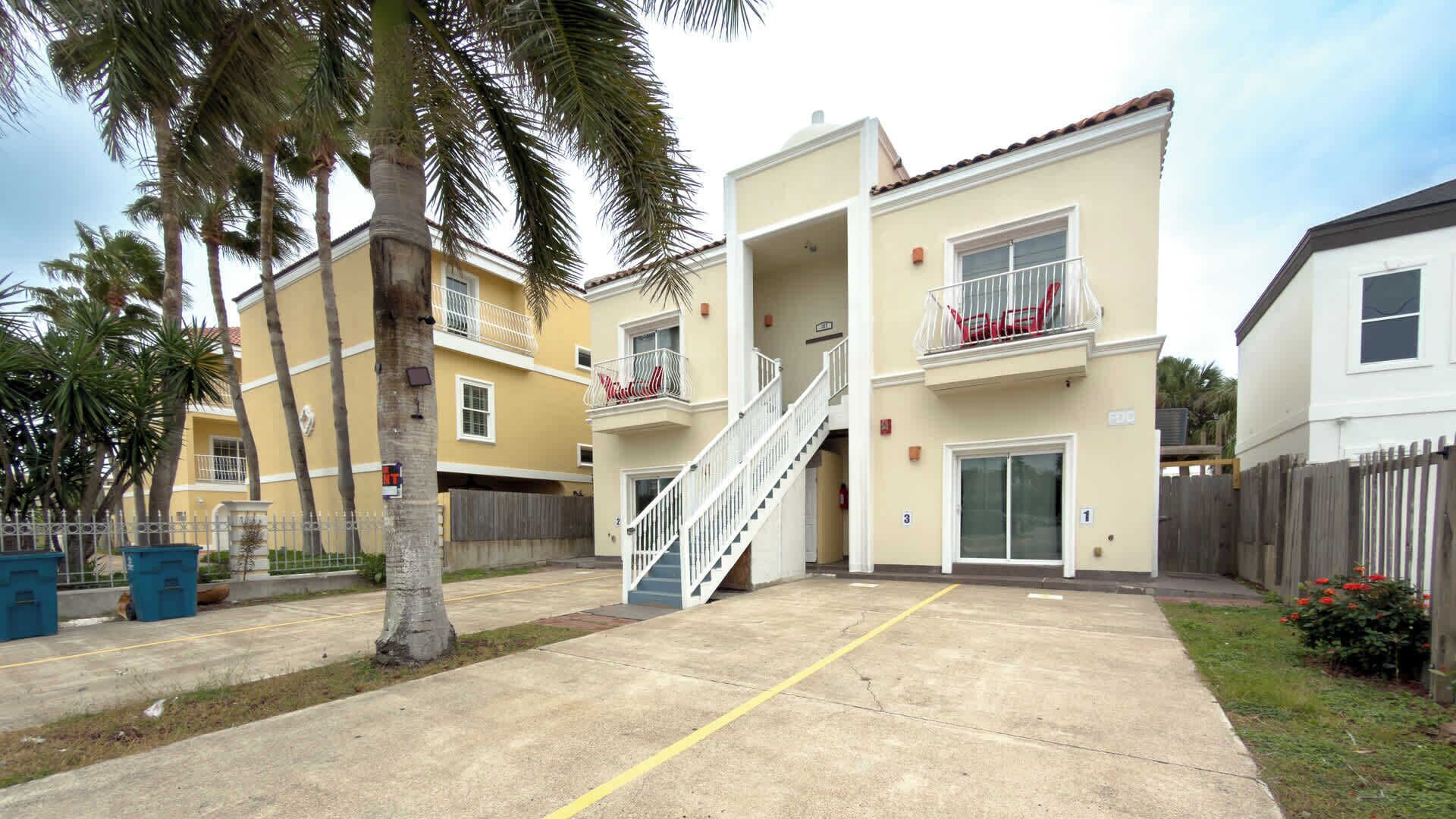 A multi-story residential building with balconies, a central staircase, and a gated driveway.