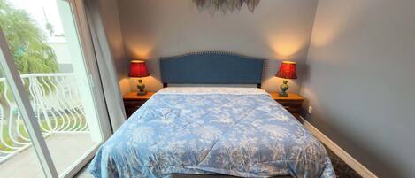 A bedroom with a bed, two bedside lamps, a bench, and a view of a balcony with a railing.