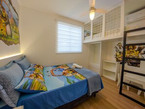 A bedroom with a bunk bed, a bed with a colorful bedspread, a ceiling fan, and a window with blinds.
