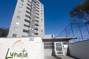 A high-rise building with balconies, a gated entrance, and a clear blue sky. - Curta Praia do Quilombo - Lunata (Penha)