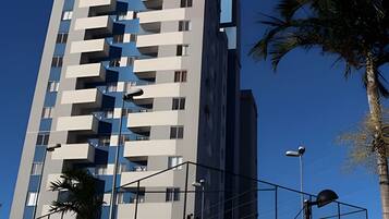 Um edifício com vários andares, varandas, um poste de luz e uma palmeira.