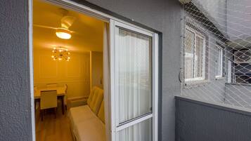 A room with a bed, a small table, and a chair. There is a window with a curtain, and a balcony with a railing.