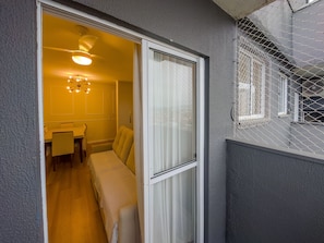 A room with a bed, a small table, and a chair. There is a window with a curtain, and a balcony with a railing. - Curta Praia do Quilombo - Lunata (Penha)