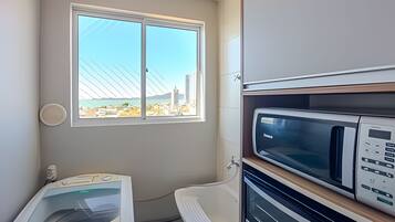 Cocina compacta con microondas, horno y ventana con vistas a edificios y un puente.