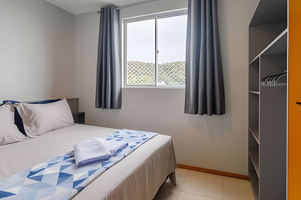 A bedroom with a bed, a window with curtains, a wardrobe, and a tiled floor.