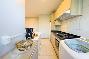 A compact kitchen with a coffee maker, a basket, a stove, and a washing machine. - Curta Praia do Quilombo - Lunata (Penha)