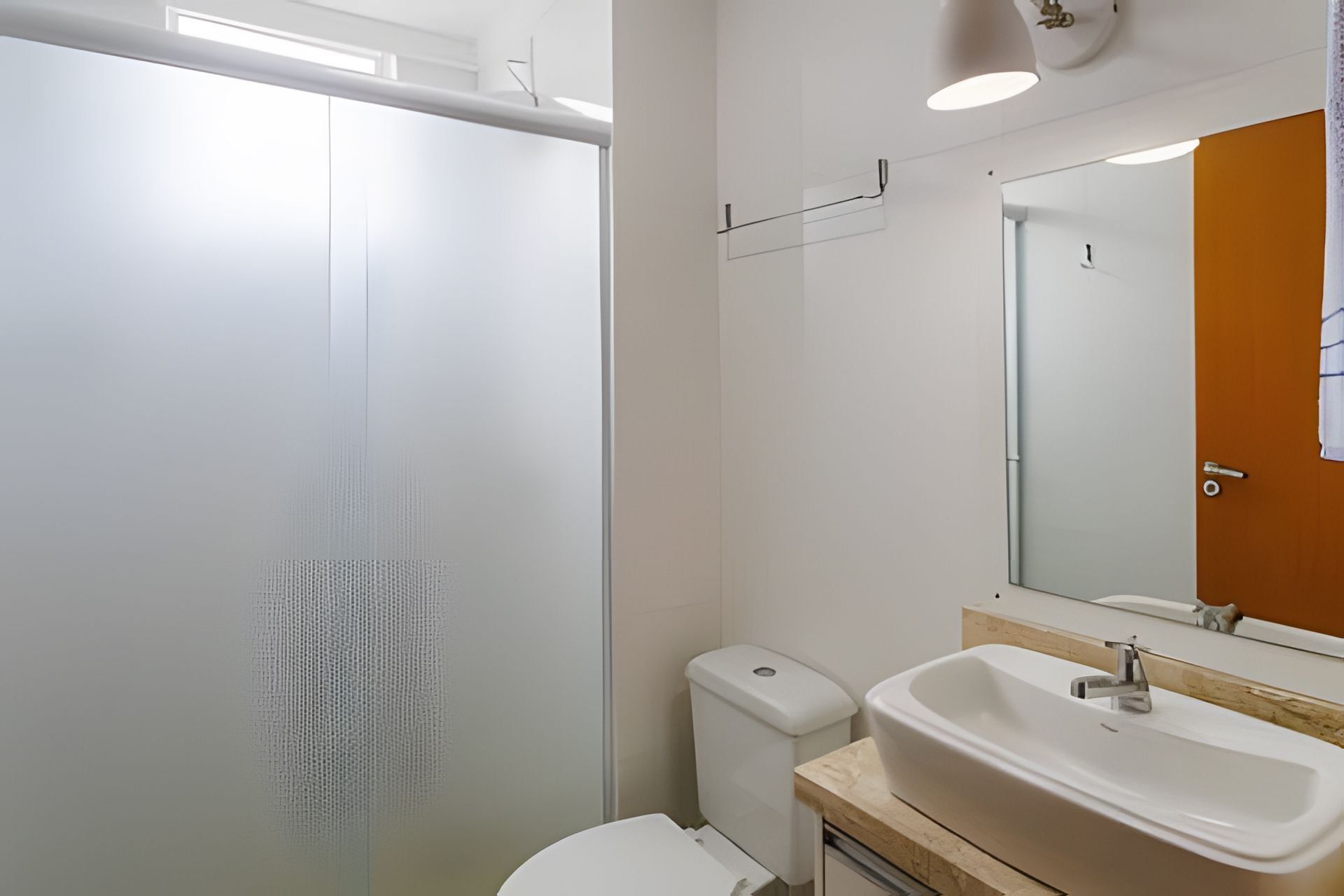 A bathroom with a glass shower enclosure, a toilet, a sink with a mirror, and a wooden countertop.