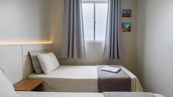 Une chambre avec deux lits, une fenêtre avec des rideaux, une table de chevet et un tableau au mur.