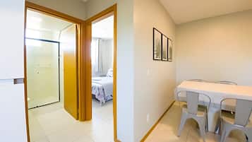 Una habitación de hotel con cama, baño, zona de comedor con mesa y sillas, y un pasillo que lleva a otra habitación.