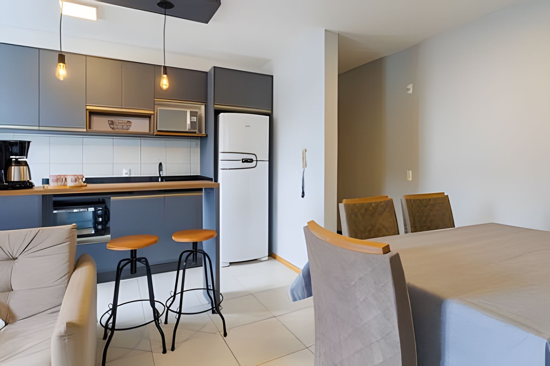 Una cocina compacta equipada con microondas, refrigerador y taburetes de bar.